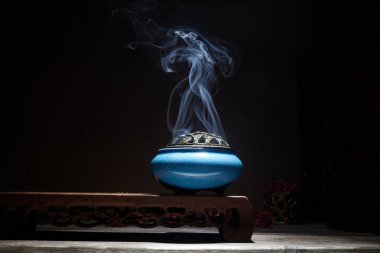 Yanan tütsü çubuklarından çıkan duman lotus tütsü tutacağının üzerinde duruyor.