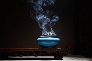 Yanan tütsü çubuklarından çıkan duman lotus tütsü tutacağının üzerinde duruyor.