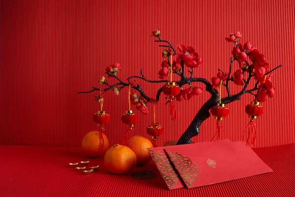 Dekorationen für das chinesische Neujahrsfest. Orange, Blatt, rotes Päckchen, Pflaumenblüte auf rotem Hintergrund. — Stockfoto
