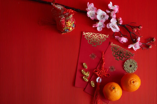 Dekorationen für das chinesische Neujahrsfest. Orange, Blatt, rotes Päckchen, Pflaumenblüte auf rotem Hintergrund. — Stockfoto