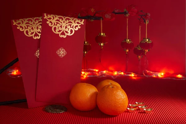 Čínská novoroční slavnostní dekorace. Pomeranč, list, červený balíček, švestkový květ na červeném pozadí. — Stock fotografie