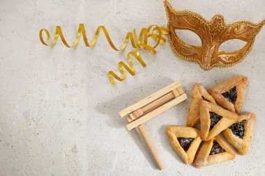 Yahudi bayramı Purim arka planında hamantaschen ya da hamans kulaklı kurabiyeler, karnaval maskesi ve gürültü çıkarıcı