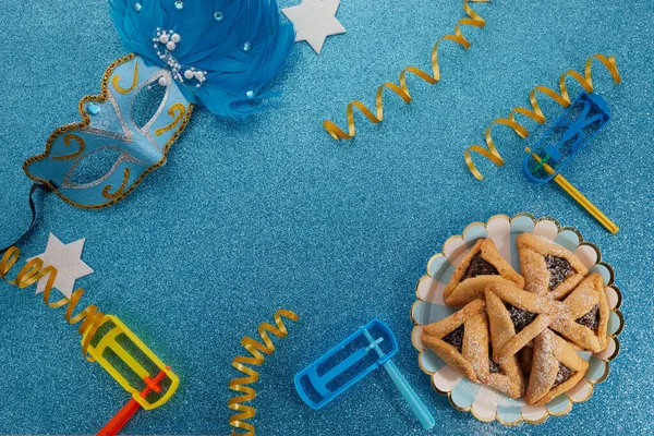 Jewish holiday Purim background with hamantaschen or hamans ears cookies, carnival mask and noisemaker — Stock Photo, Image