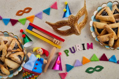 Yahudi bayramı Purim arka planında hamantaschen ya da hamans kulaklı kurabiyeler, karnaval maskesi ve gürültü çıkarıcı