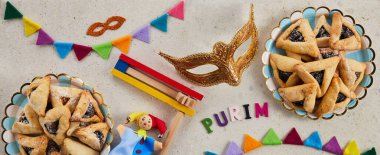 Yahudi bayramı Purim arka planında hamantaschen ya da hamans kulaklı kurabiyeler, karnaval maskesi ve gürültü çıkarıcı