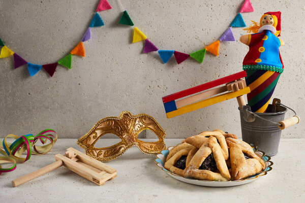 Jewish holiday Purim background with hamantaschen or hamans ears cookies, carnival mask and noisemaker