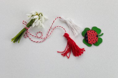Beyaz zemin üzerinde kırmızı ve beyaz ip ve lalybug ile bir buket kar damlası. Mart ayının ilk kutlamaları Martisor.