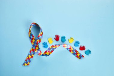 Renkli kurdeleli ve mavi arka planda elleri olan otizm farkındalığı kavramı. Üst görünüm