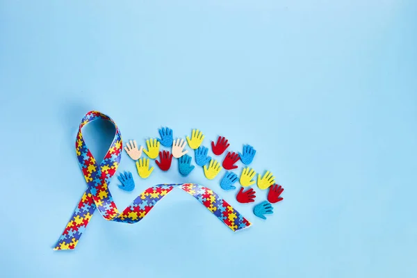 Autisme bewustzijn concept met kleurrijk lint en handen op blauwe achtergrond. Bovenaanzicht — Stockfoto