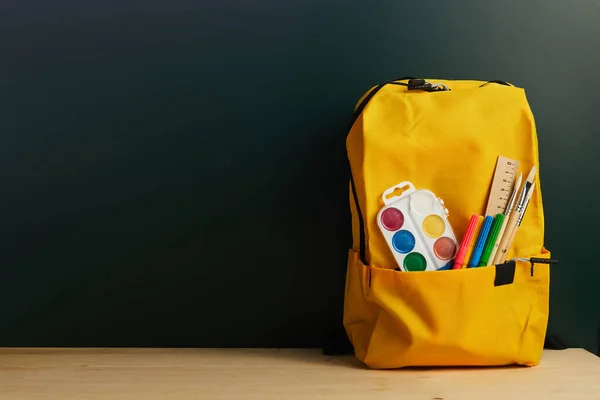 School backpack with colorful school supplies on table