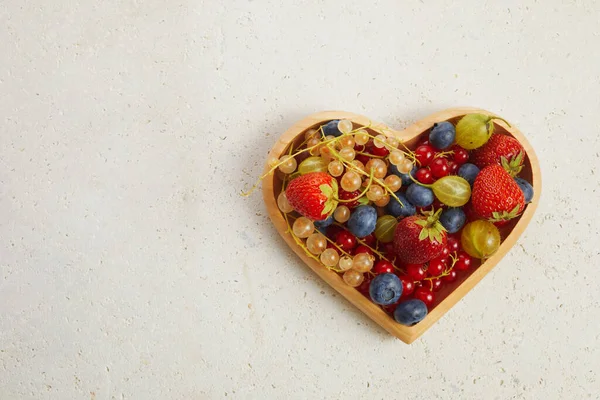 Berries mix in in a heart shaped bowl on travertine background.