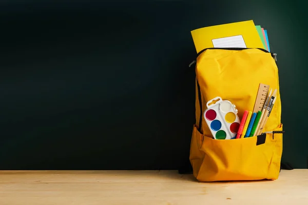 School backpack with colorful school supplies on table