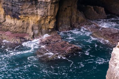 Canlı turkuaz okyanus dalgaları kayalara çarpıyor.