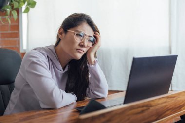Mexican woman with home office is bored and sleepy in front of the computer