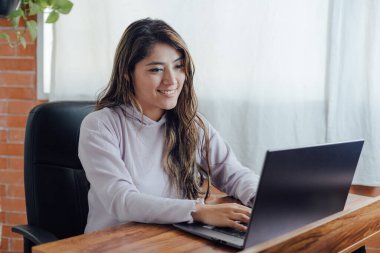 Mexican woman with home office works happy in front of computer