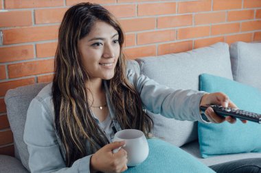 Mexican woman points with the control of the television. home entertainment