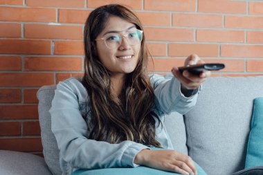 Mexican woman points with the television control smiles when watching a movie