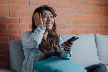Mexican woman points with the television control smiles when watching a movie