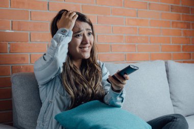 Mexican woman points with the television control smiles when watching a movie