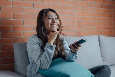 Mexican woman points with the television control smiles when watching a movie