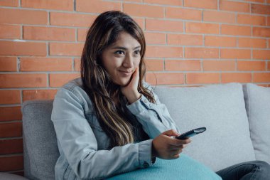 Mexican woman points with the television control smiles when watching a movie