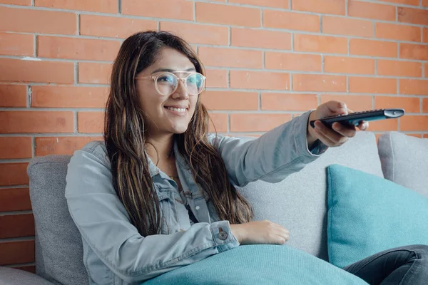 Mexican woman points with the control of the television. home entertainment