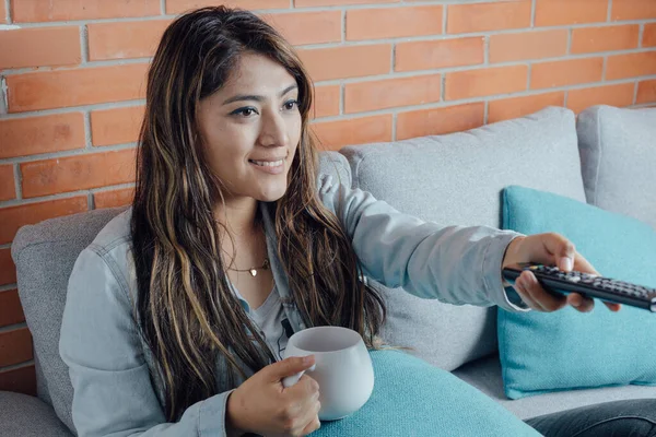 Mexican woman points with the control of the television. home entertainment