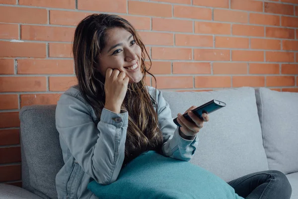 Mexican woman points with the television control smiles when watching a movie