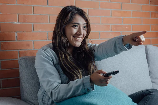 Mexican woman points with the television control smiles when watching a movie