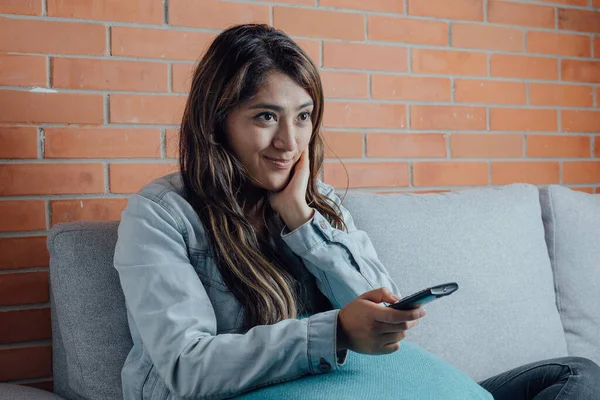 Mexican woman points with the television control smiles when watching a movie