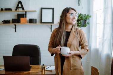 Meksikalı genç bir kadın, ofisinde doğal duruşu olan beyaz bir bardaktan içiyor.