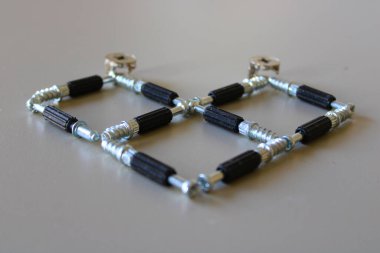 Bej masanın üzerinde duran vidalardan yapılmış bir kalp. Kalp üç dik kareden oluşur..