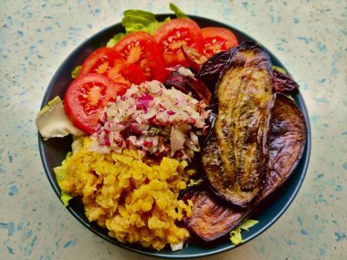 Kızarmış patlıcan, domates, lahana ve siyah tabakta servis edilen kırmızı mercimek. Tabak mavi köşeli mutfak masasında duruyor..