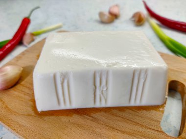 Kesme tahtasının üzerinde kırmızı biber, soğan ve arka planda sarımsaklı beyaz soya peyniri..