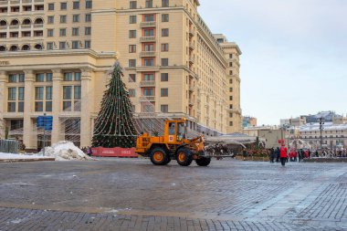 Moskova, Rusya - 28 Aralık 2021 Moskova Oteli önünde kar temizleme. Kar temizleme için turuncu traktör, çelenkli Noel ağacı.
