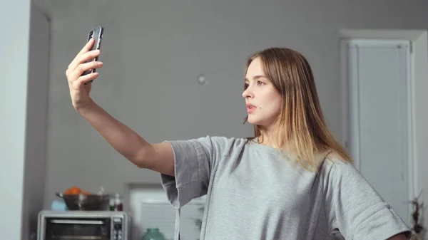 Uma menina com um telefone em suas mãos leva uma selfie — Fotografia de Stock