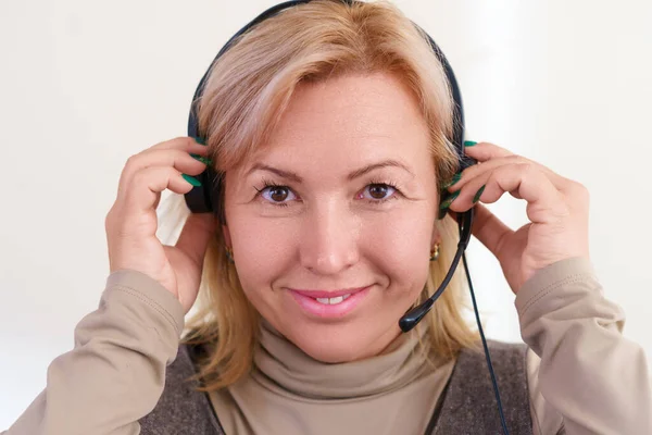 Uśmiechnięta biała kobieta w średnim wieku zakłada słuchawki. Koncepcja biura. — Zdjęcie stockowe