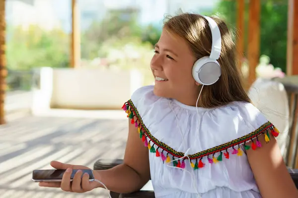 Kanepede akıllı telefonuyla oturan, kulaklıkla müzik dinleyen gülümseyen bir kız. Metin için boşluk.