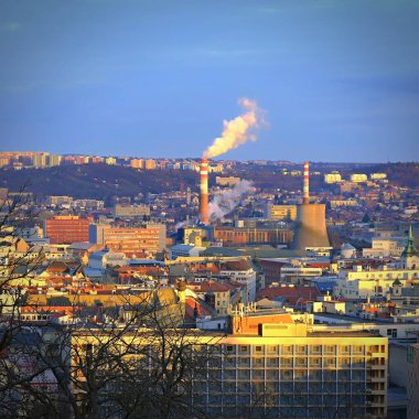 Şehirde evleri olan bacaları buharlaştırmak. Çevre ve endüstri kavramı. Gün batımında şehir manzaralı bir arka plan. Brno - Çek Cumhuriyeti - Avrupa.