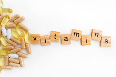 Farklı hapların beyaz arka planında tahta küplere kazınmış vitaminler.