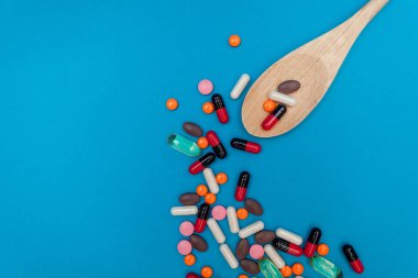 mavi arka planda tahta kaşıkta çok renkli haplar.