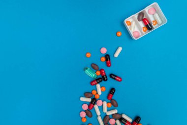 Mavi arka planda çok renkli hapları olan ilaç dağıtıcısı.