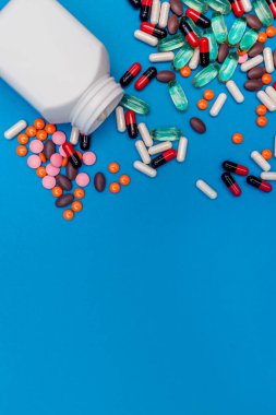 Mavi arka planda kavanozdan düşen çok renkli haplar.