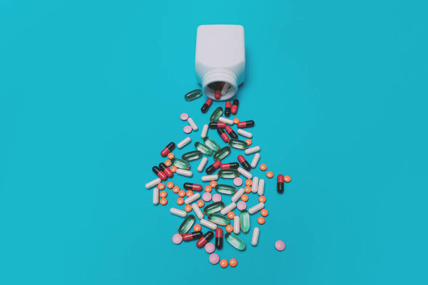разноцветные таблетки, падающие из банки на голубом фоне
