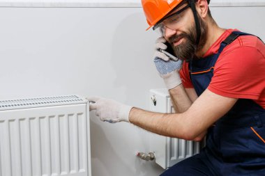 Turuncu kasklı bir işçi eve radyatör yerleştirir.