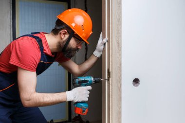Turuncu kasklı matkaplı bir işçi eve bir kapı yerleştirir.