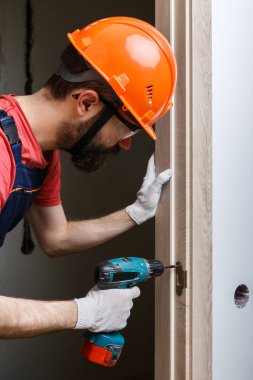 Turuncu kasklı matkaplı bir işçi eve bir kapı yerleştirir.