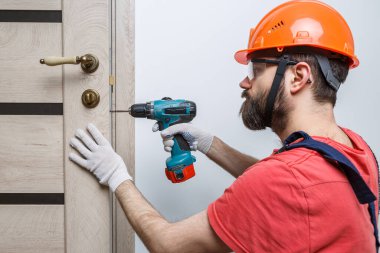 Turuncu kasklı matkaplı bir işçi eve bir kapı yerleştirir.