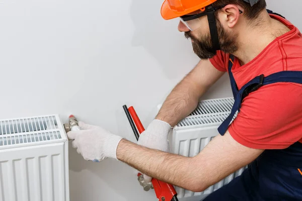 Turuncu kasklı bir işçi eve radyatör yerleştirir.