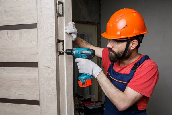 Turuncu kasklı matkaplı bir işçi eve bir kapı yerleştirir.